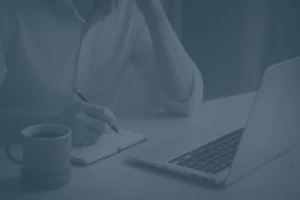 Wholesale buyer writing notes beside silver laptop and coffee at desk