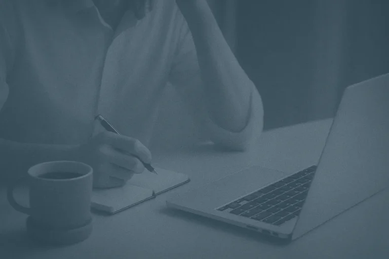 Wholesale buyer writing notes beside silver laptop and coffee at desk