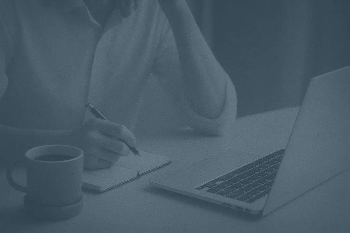 Wholesale buyer writing notes beside silver laptop and coffee at desk