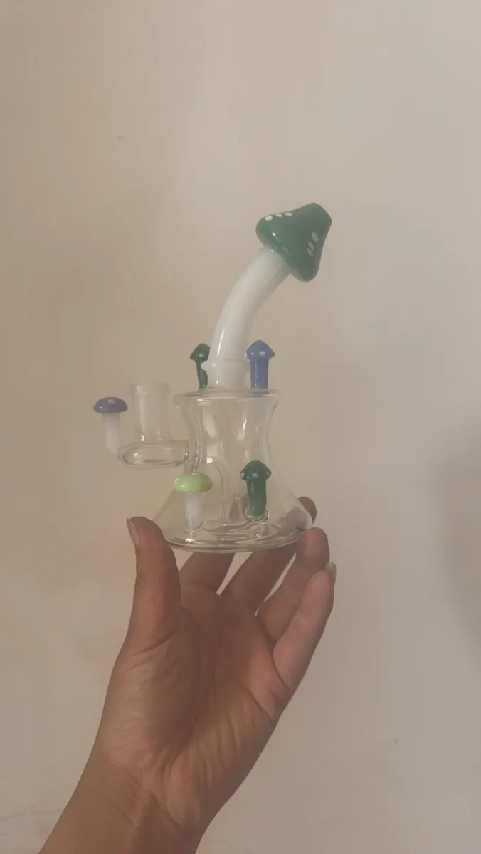 Hand holding small glass bong decorated with green blue purple mushrooms